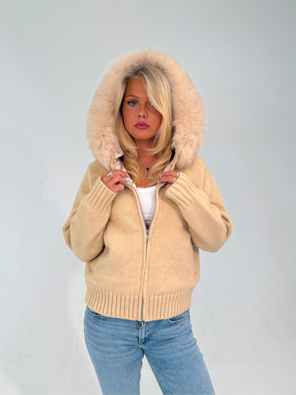 Woman wearing a beige hoodie with a fur-lined hood on a plain background