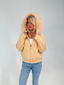 Woman wearing a beige cardigan with a fur-lined hood against a plain background