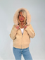 Woman wearing a beige hoodie with a fur-lined hood on a plain background